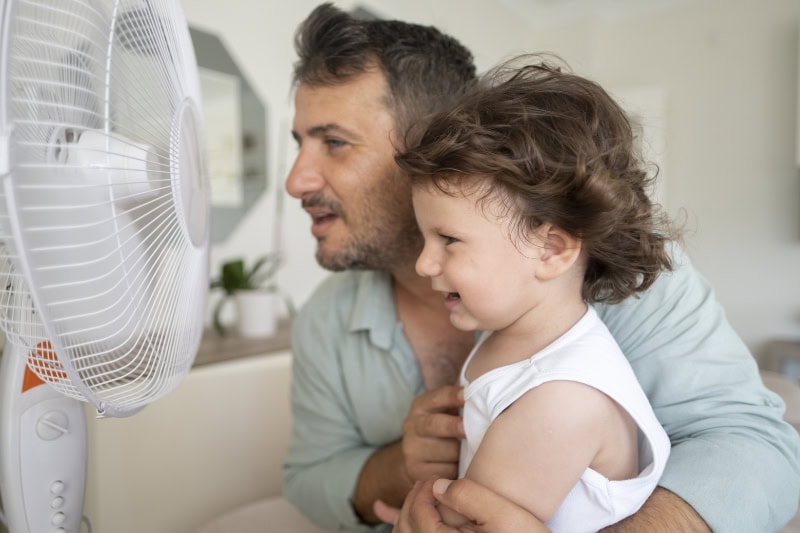 Father and toddler sitting in front of a fan.
