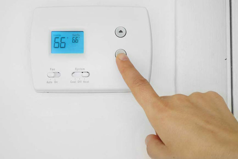 Person's hand adjusting a wall mounted thermostat temperature